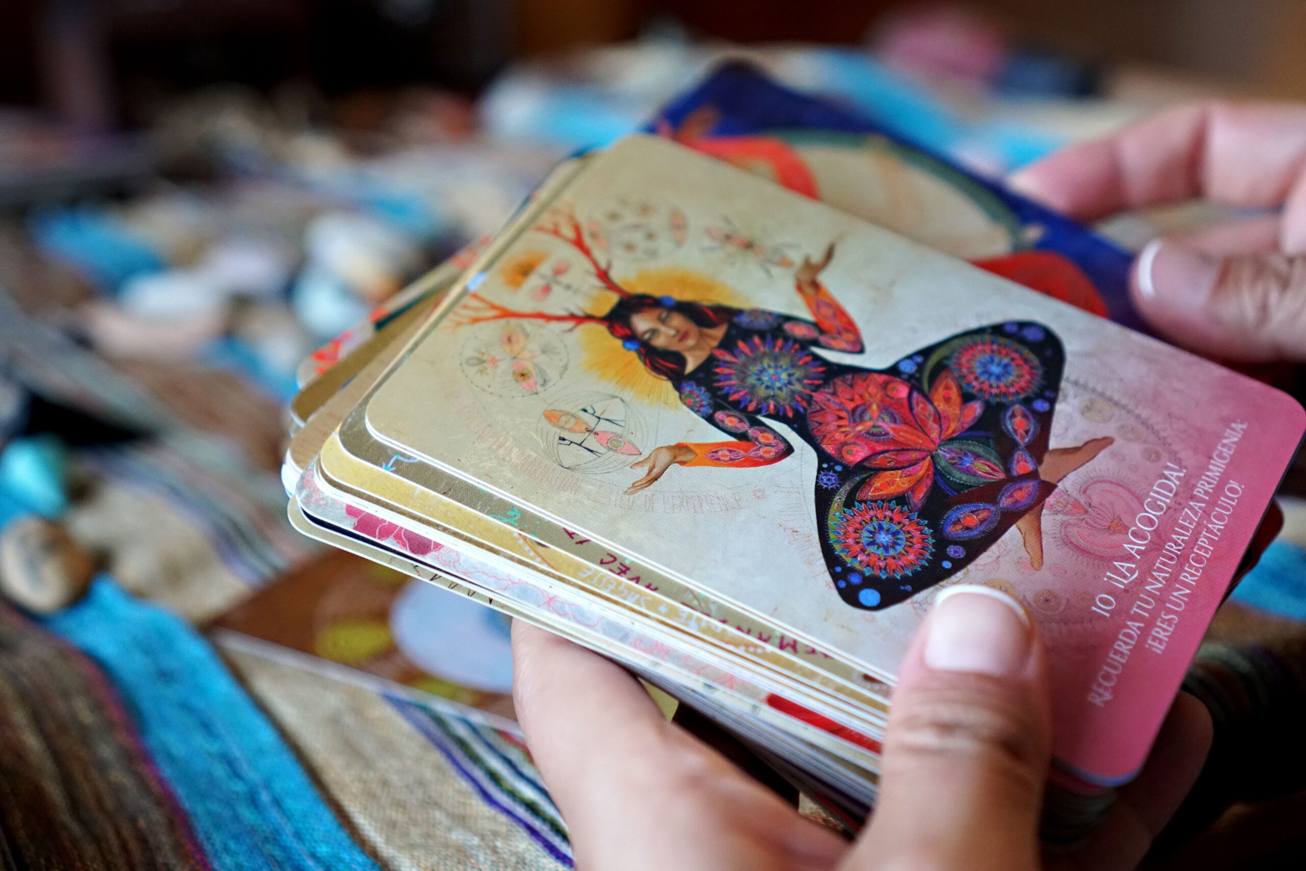 Vibrant tarot cards featuring artistic designs, held by diverse hands, indoors.
